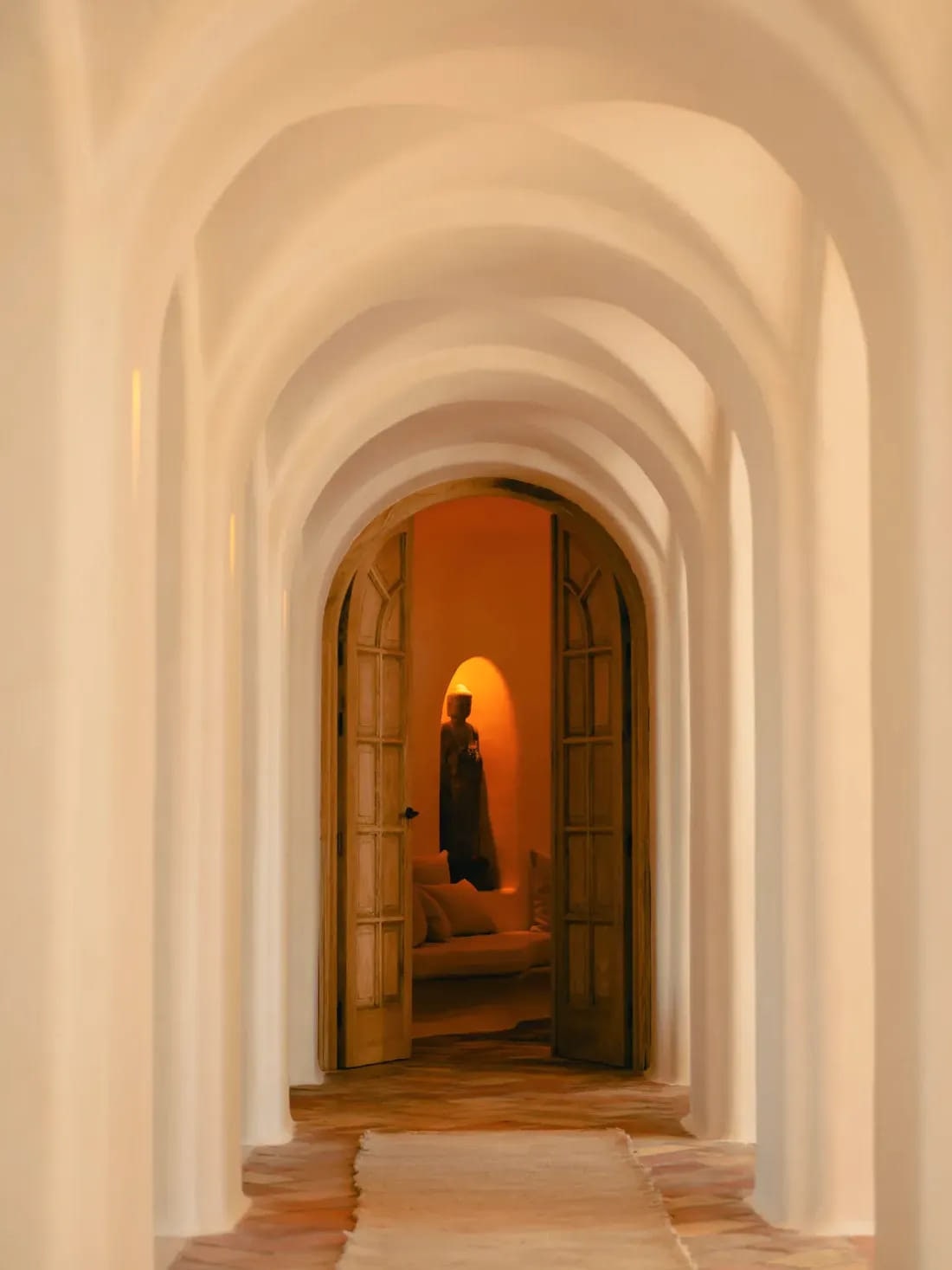 A vaulted limewashed corridor at Viluz opening onto a warm doorway at its end.