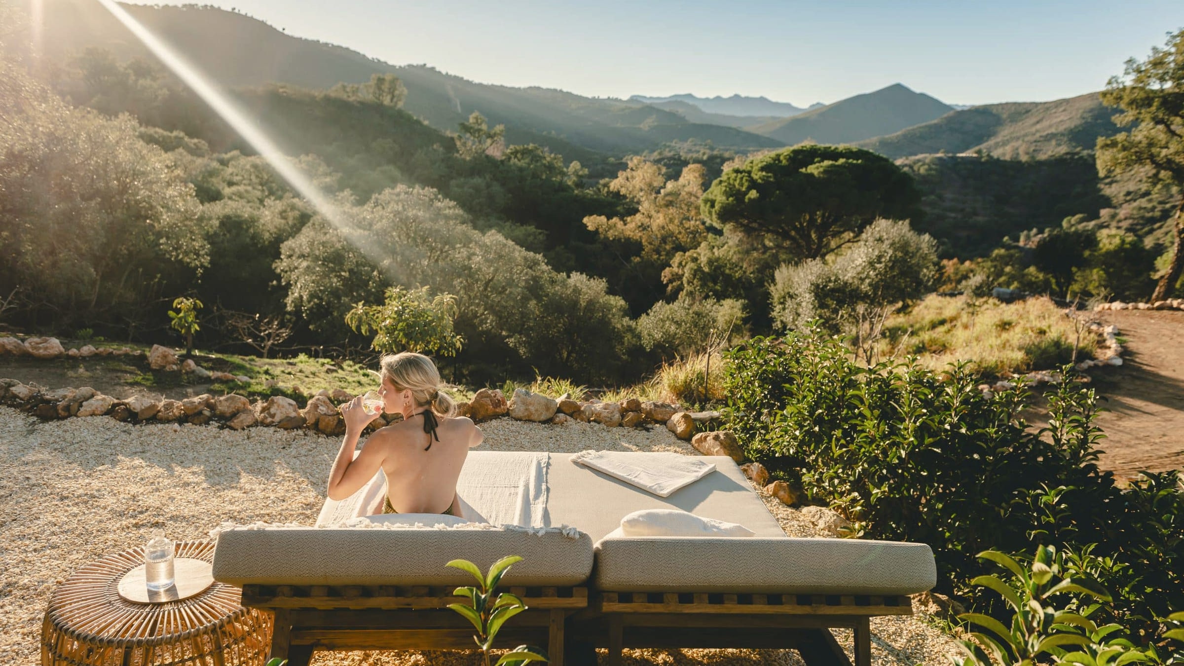 A daybed on the terrace at Viluz looking down the valley, sun flaring over the ridge beyond.