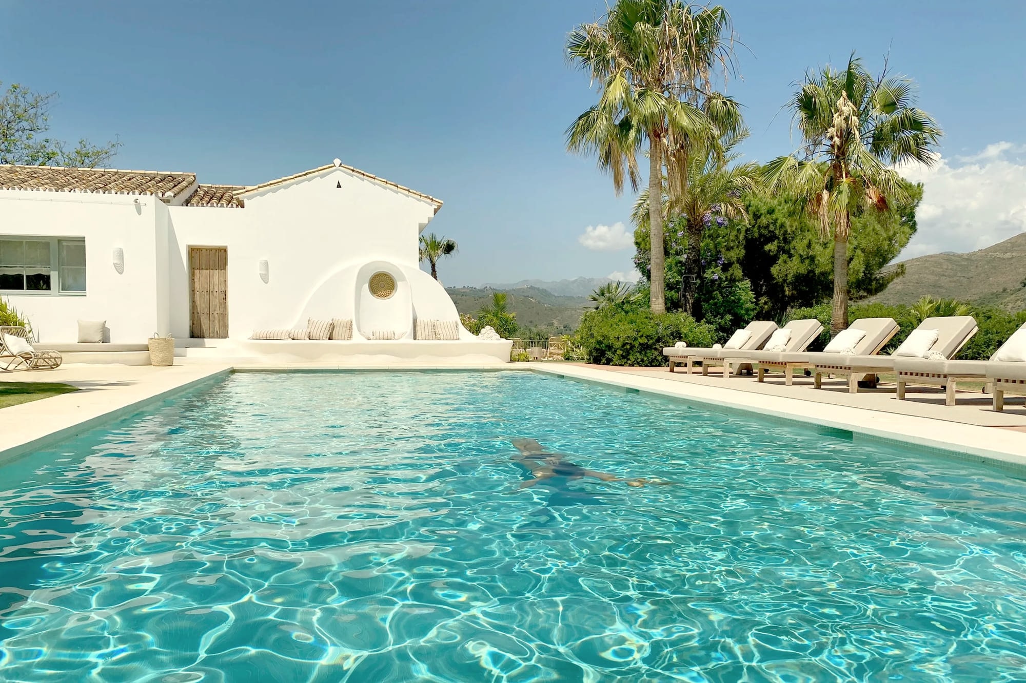 The pool at Viluz below the white house, palms and loungers along its edge.