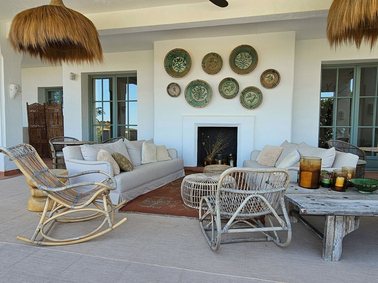 A limewashed sitting room at Viluz with rattan chairs, a low table and a fireplace laid ready.