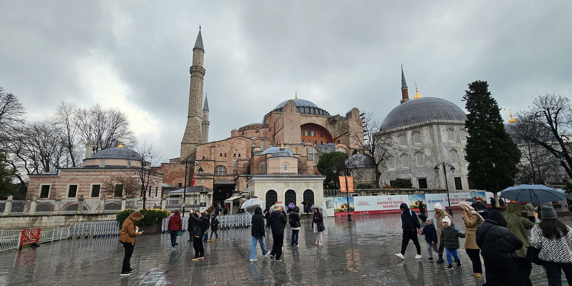 The square outside Hagia Sophia in the rain, minarets and domes behind a crowd under umbrellas.