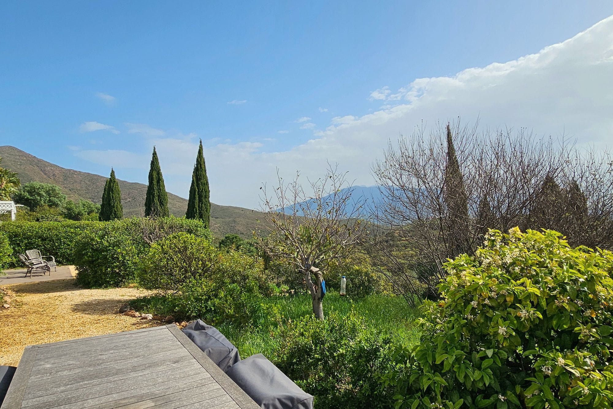 The gardens at Viluz: clipped hedges, cypresses and a gravel path, the sierra rising behind.